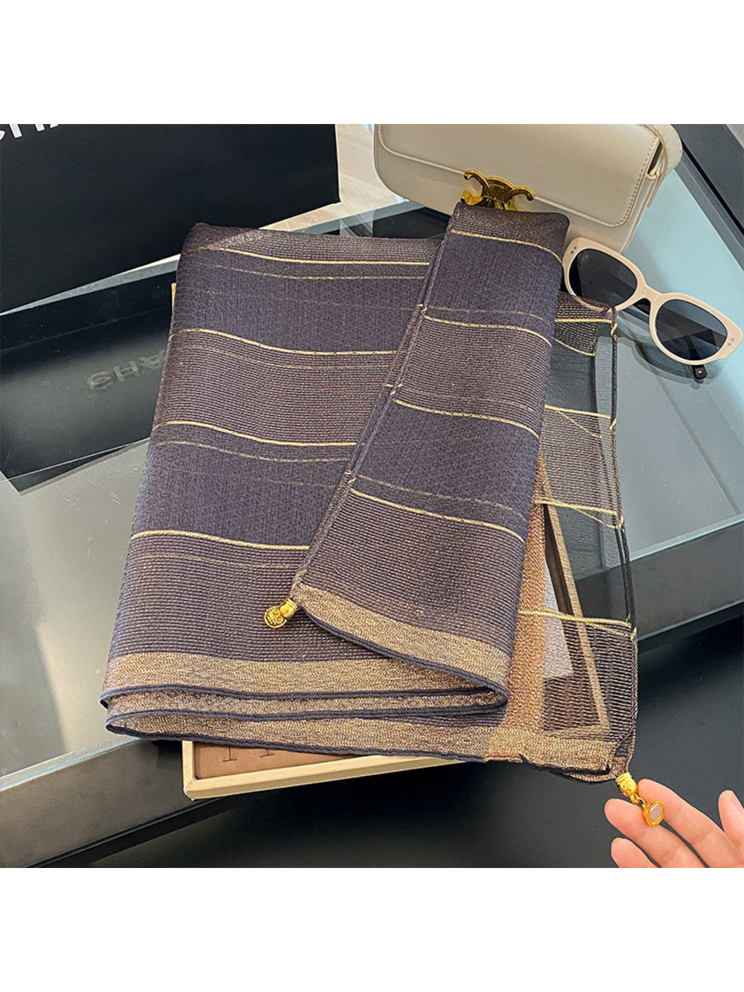Gray scarf folded on a tray with metallic-look lines and gold-tone end ornaments