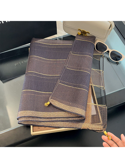 Gray scarf folded on a tray with metallic-look lines and gold-tone end ornaments
