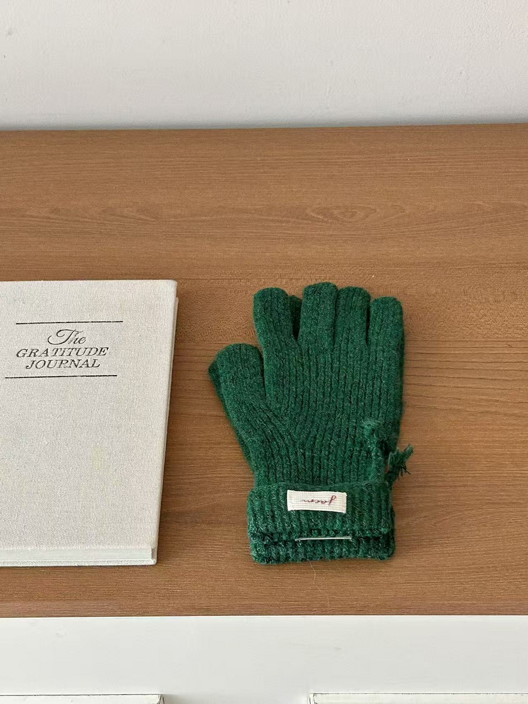 Green ribbed gloves with folded cuffs beside a journal
