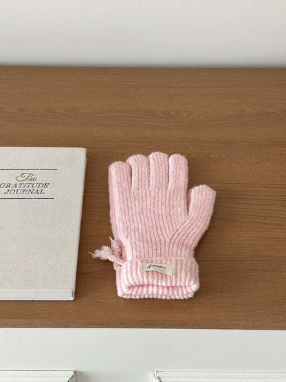 Pink ribbed gloves with folded cuffs beside a journal