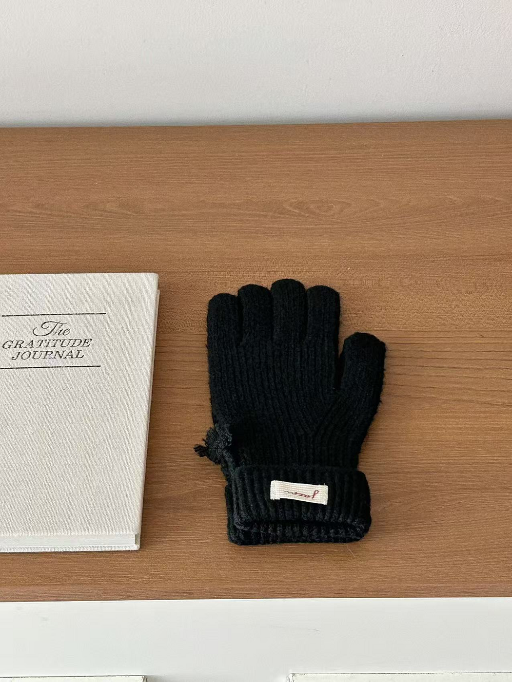 Black ribbed gloves with folded cuffs beside a journal