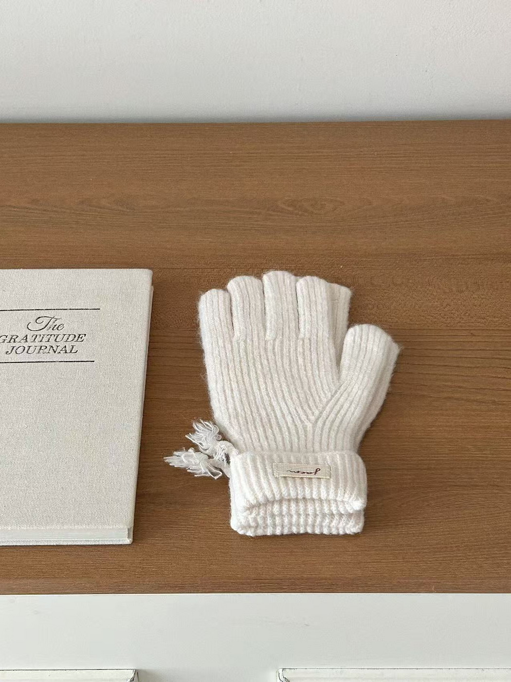 Ivory ribbed gloves with folded cuffs beside a journal