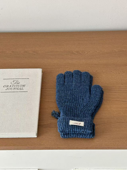 Navy ribbed gloves with folded cuffs beside a journal