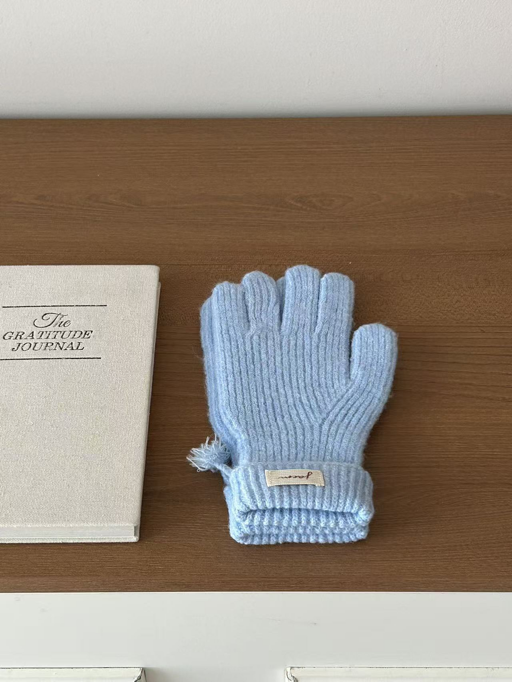 Blue ribbed gloves with folded cuffs beside a journal