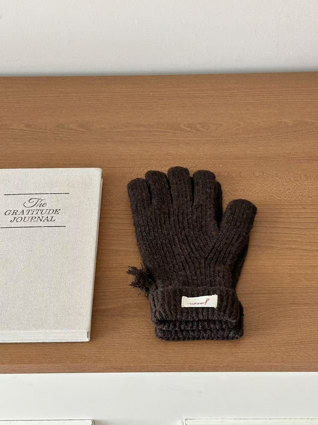 Coffee ribbed gloves with folded cuffs beside a journal