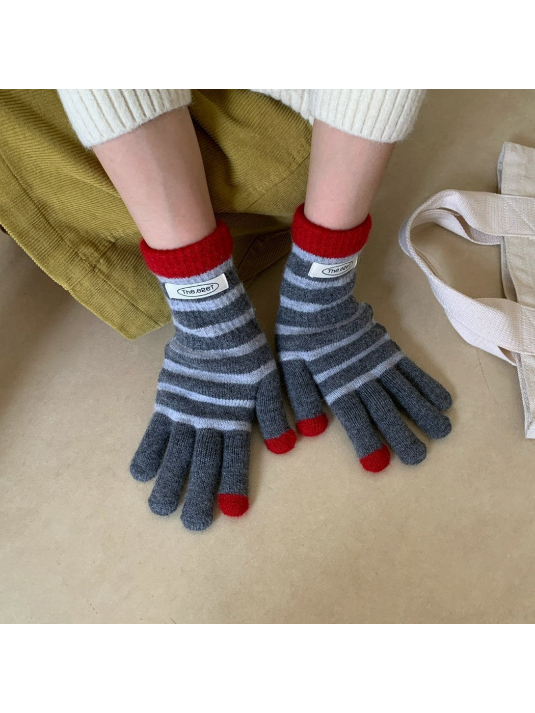 Gray striped gloves with red cuffs worn side by side