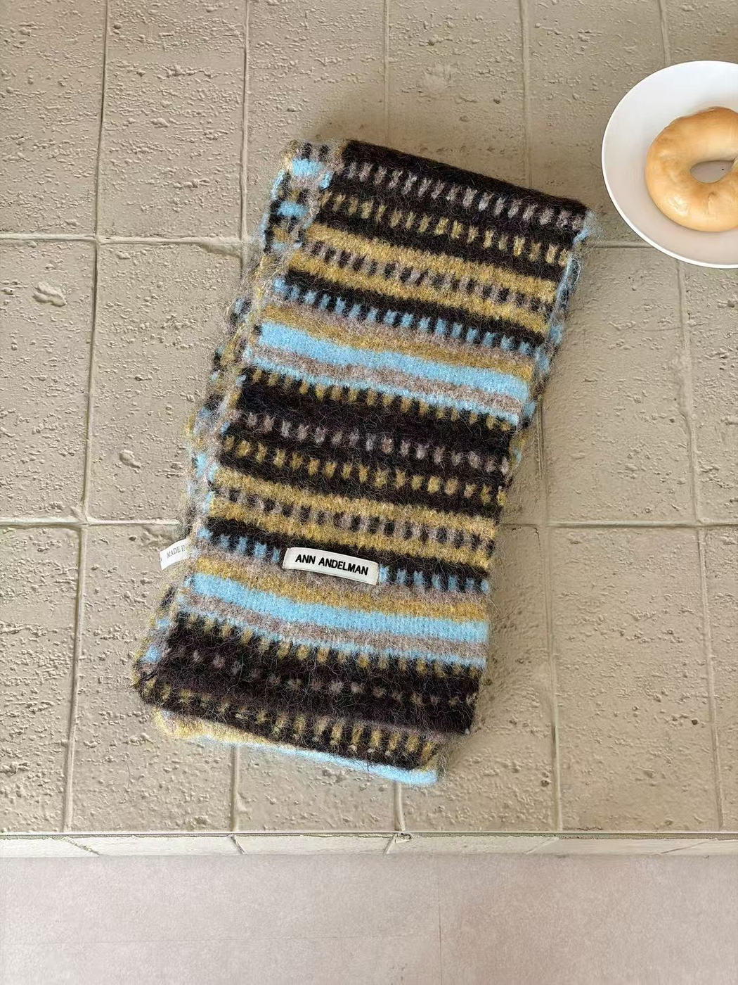 Brown scarf folded lengthwise, with light blue, mustard and gray stripes and contrasting dash rows
