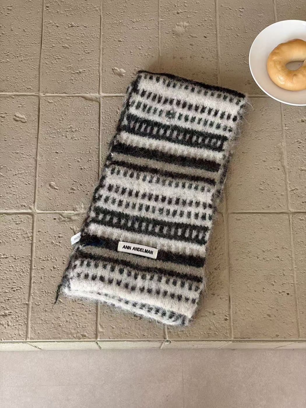 White scarf folded lengthwise, with dark and gray stripes and contrasting dash rows