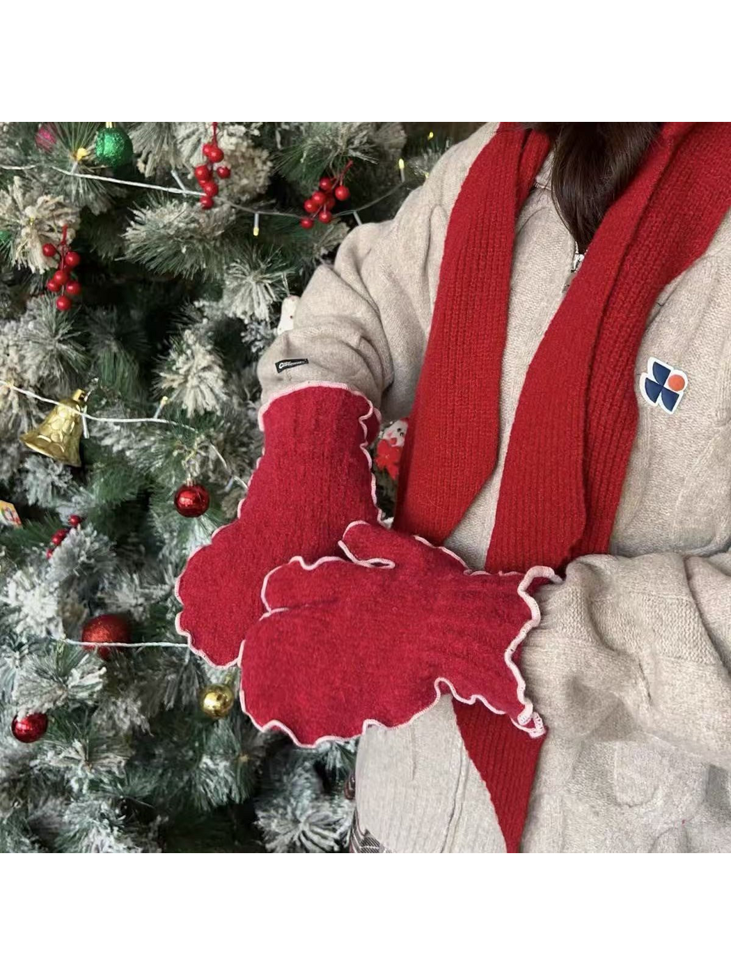 Red mittens with pale ruffled edging worn beside a decorated tree