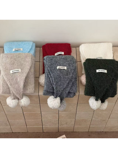 Six scarf colors displayed in two rows with knit texture, attached labels and contrasting pom-poms