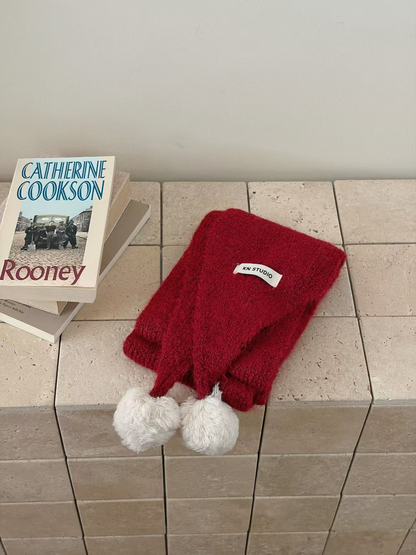 Red knit scarf folded with two off-white pom-poms and an attached label