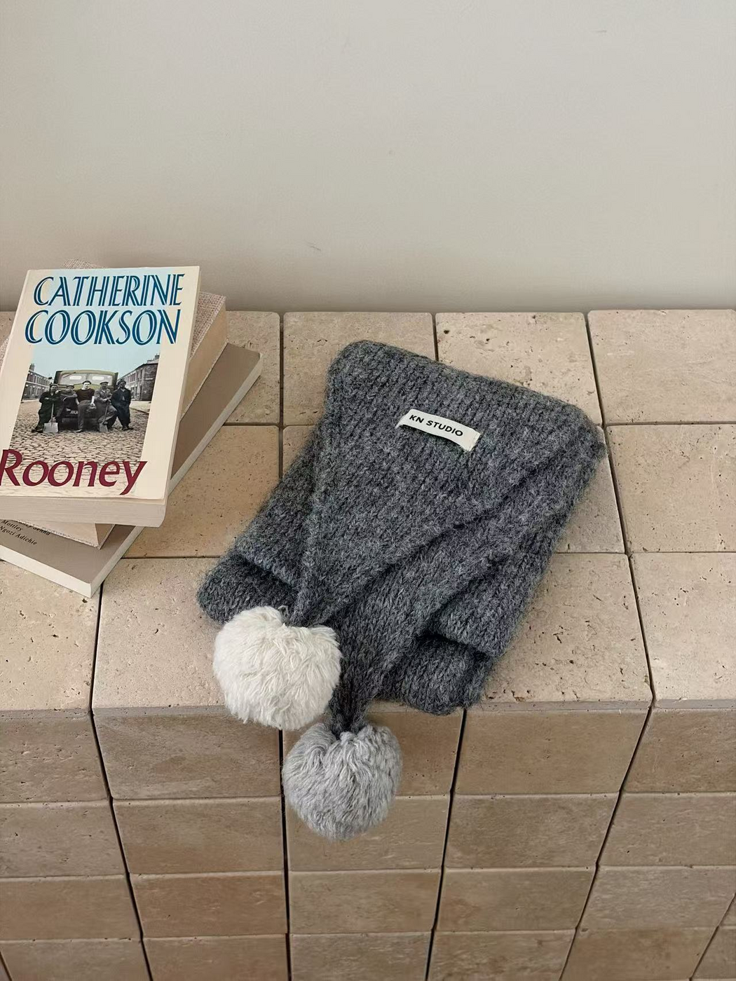 Gray knit scarf folded with one off-white and one light gray pom-pom