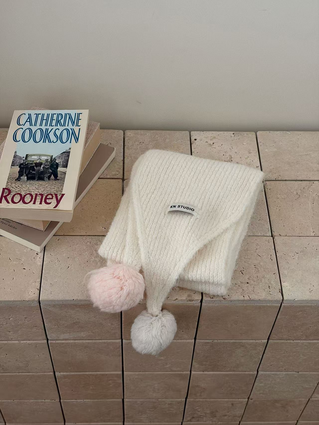 White knit scarf folded with one white and one light pink pom-pom