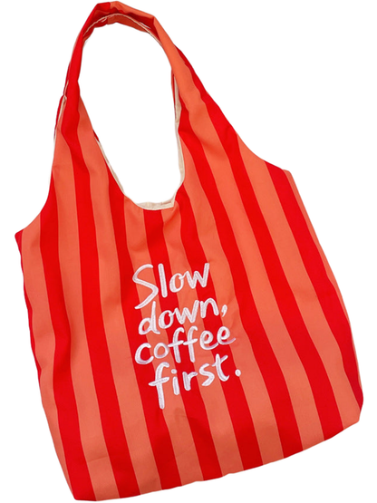 Red tote bag with broad vertical stripes and white slogan lettering, laid flat