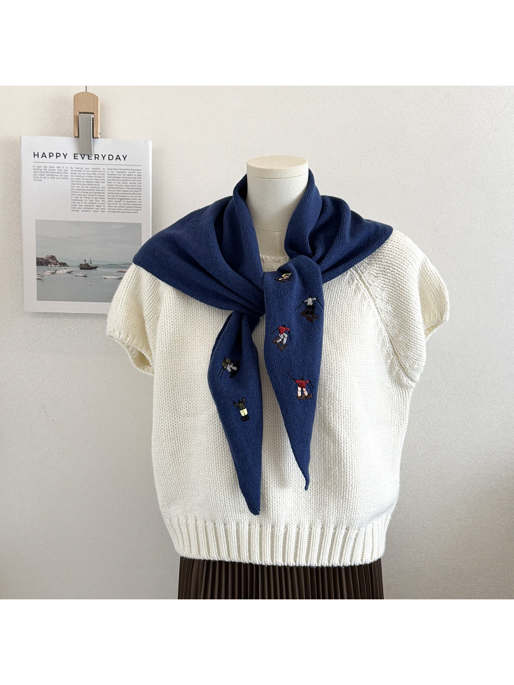 Navy knit scarf with embroidered winter-sport figures, tied over a white top