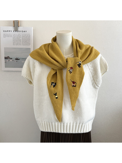 Mustard knit scarf with embroidered winter-sport figures, tied over a white top