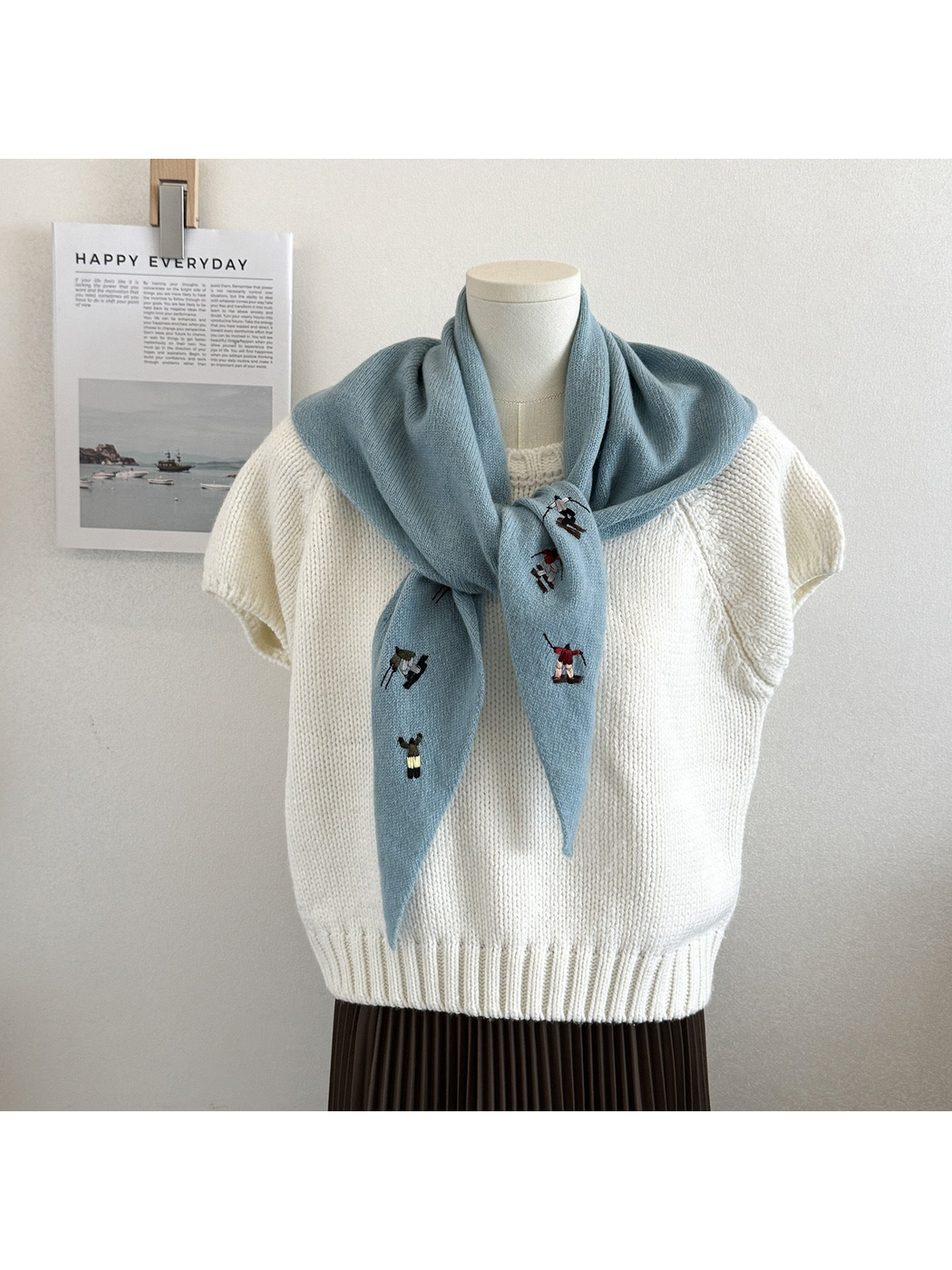 Lake Blue knit scarf with embroidered winter-sport figures, tied over a white top
