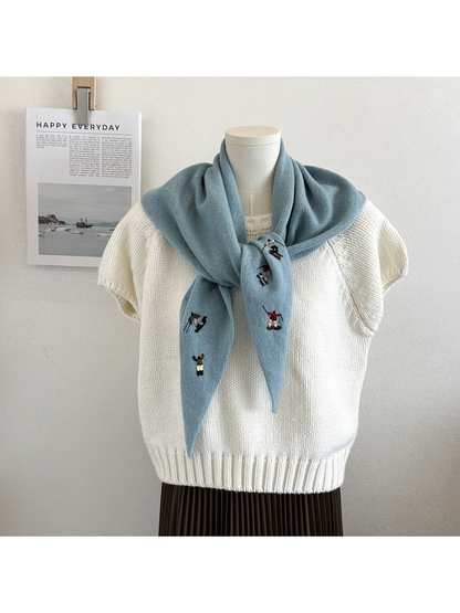 Lake Blue knit scarf with embroidered winter-sport figures, tied over a white top