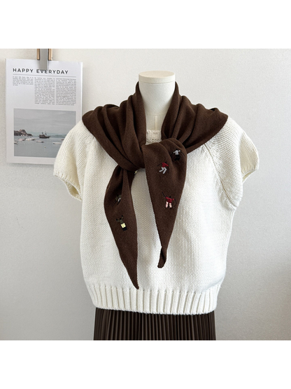 Brown knit scarf with embroidered winter-sport figures, tied over a white top