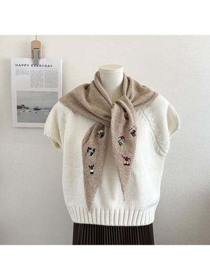 Beige knit scarf with embroidered winter-sport figures, tied over a white top