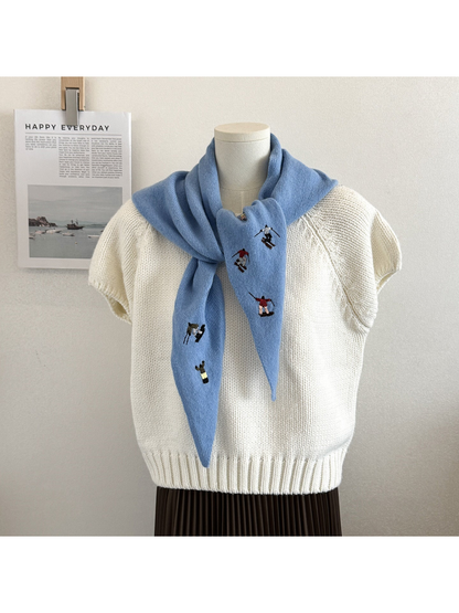 Sky Blue knit scarf with embroidered winter-sport figures, tied over a white top