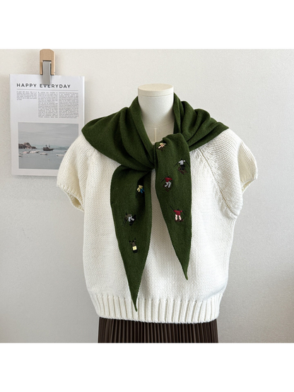 Green knit scarf with embroidered winter-sport figures, tied over a white top