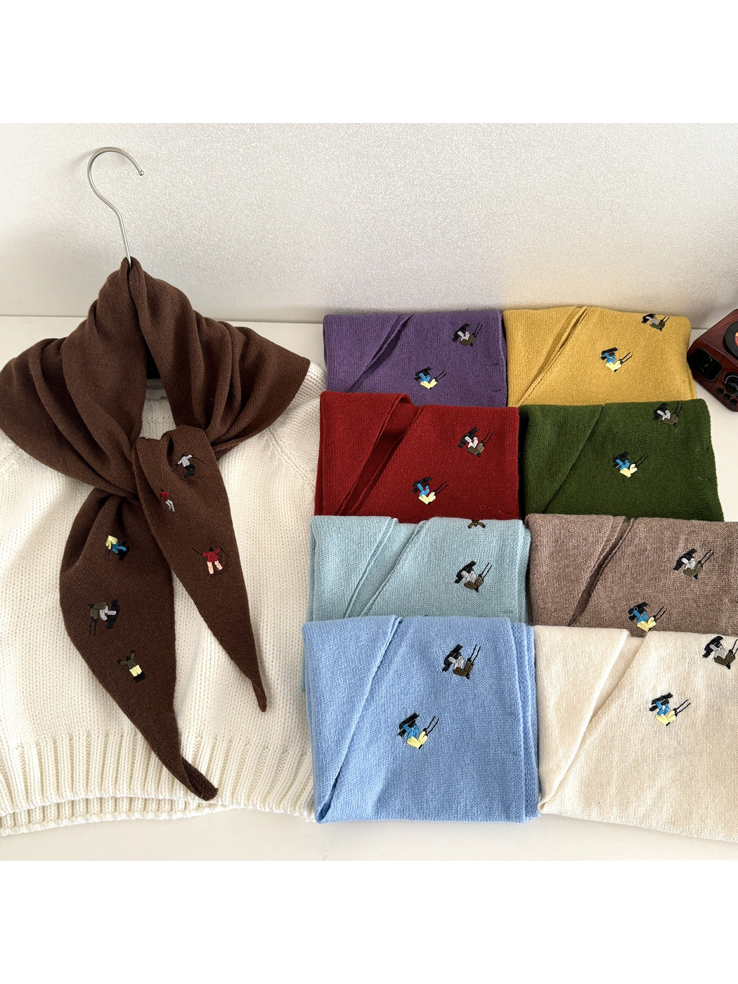 Embroidered knit scarf tied over a white top beside folded scarves