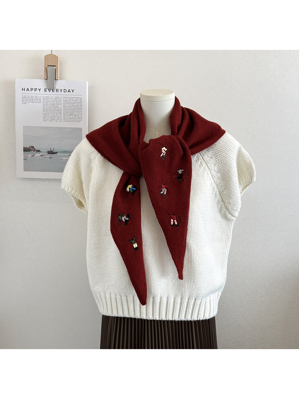 Burgundy knit triangle scarf with embroidered figures, tied on a mannequin