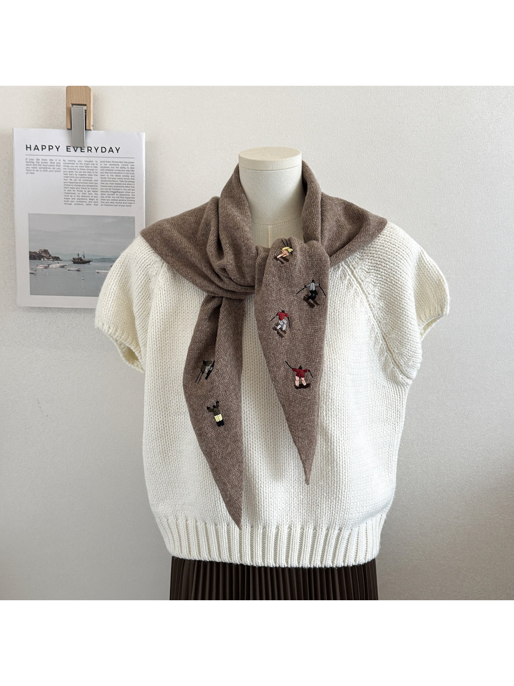 Light Coffee knit triangle scarf with embroidered figures, tied on a mannequin