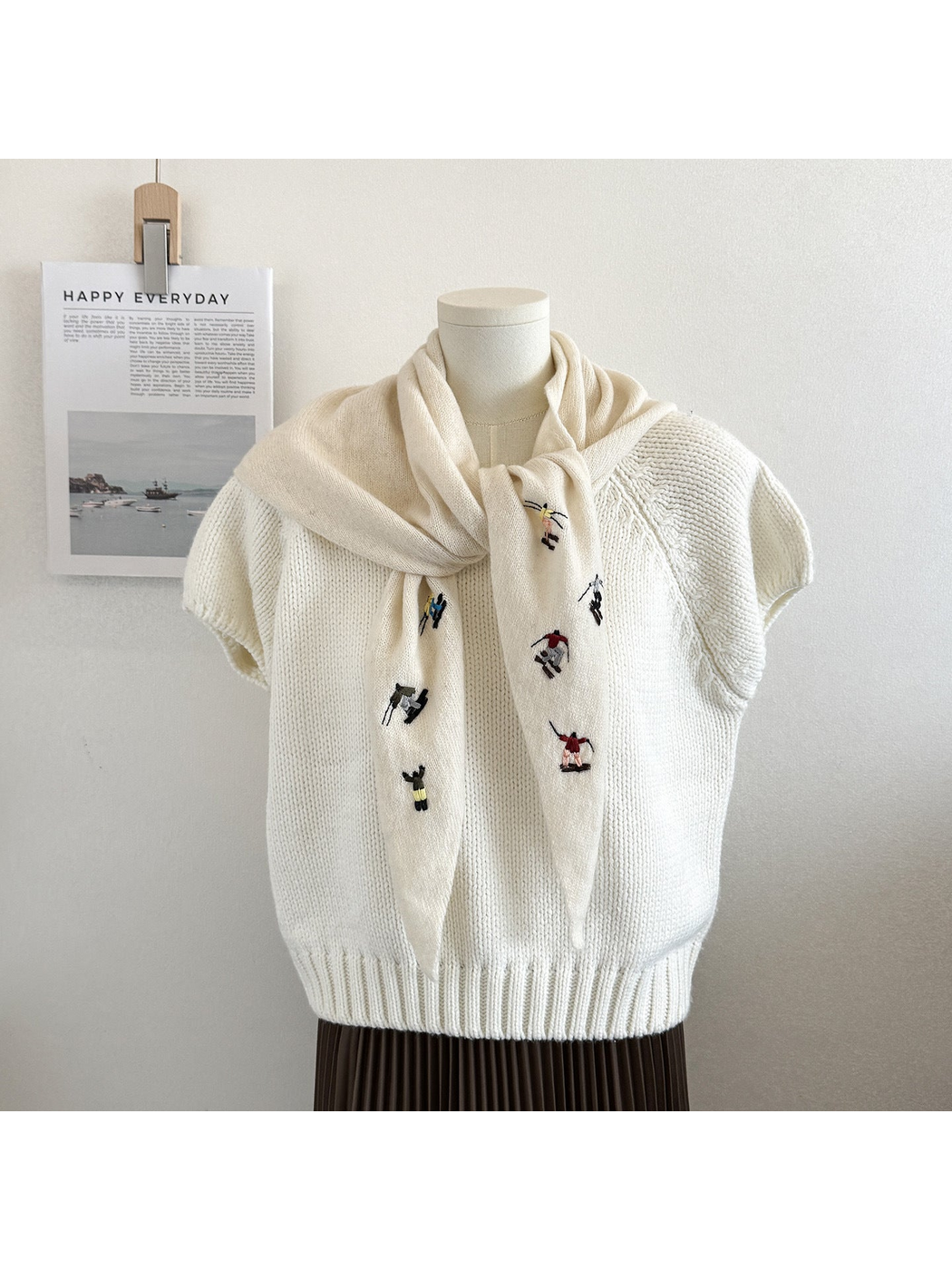 Ivory knit triangle scarf with embroidered figures, tied on a mannequin