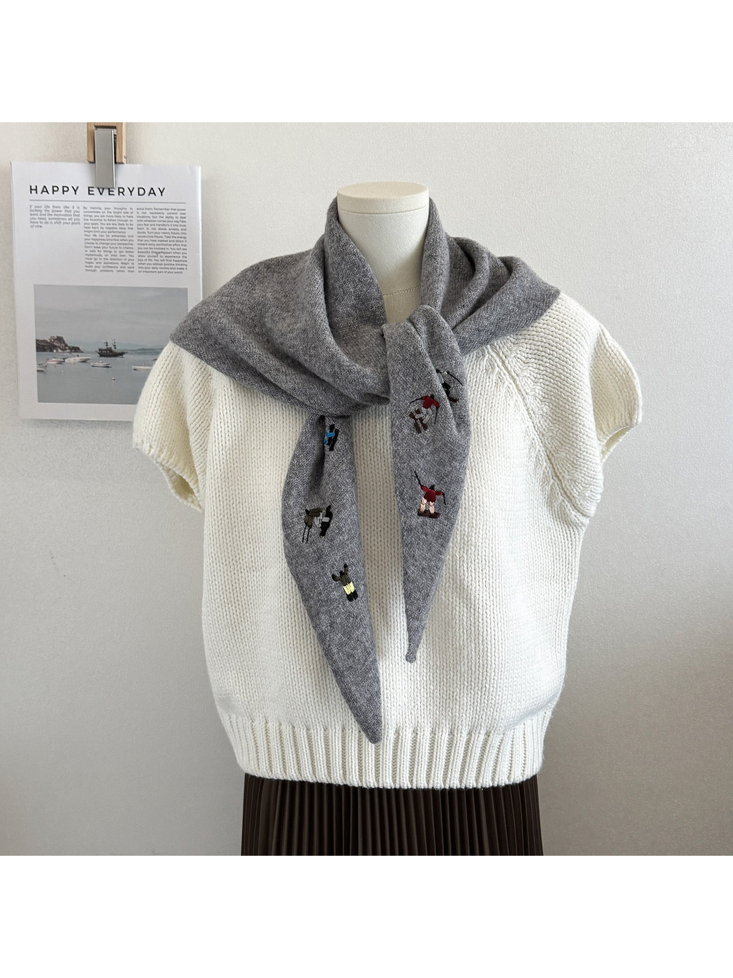Gray knit triangle scarf with embroidered figures, tied on a mannequin