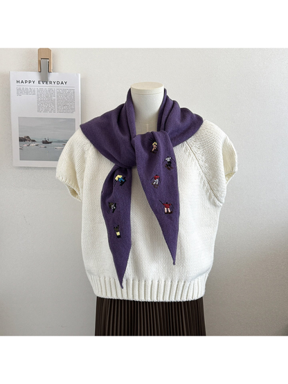Purple knit triangle scarf with embroidered figures, tied on a mannequin