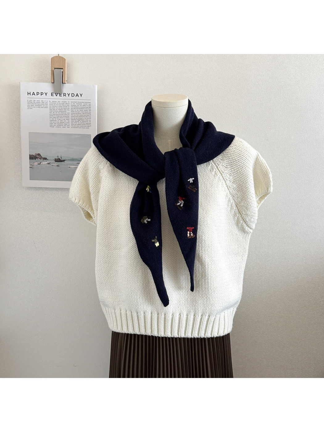 Navy knit triangle scarf with embroidered figures, tied on a mannequin