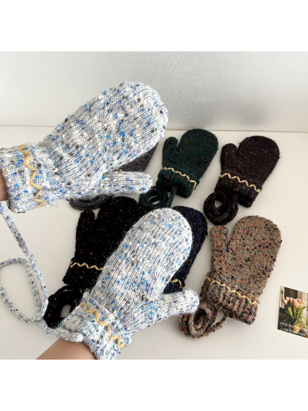 Flecked mittens worn on hands, showing knit texture and cream zigzag cuffs