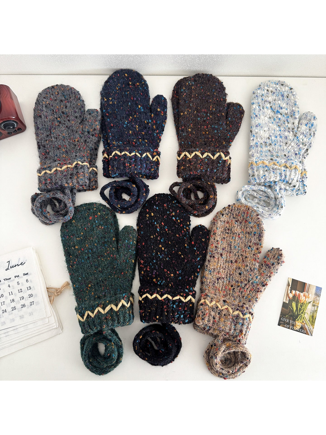 Flecked mittens in multiple colors arranged with folded cuffs and coiled connecting cords