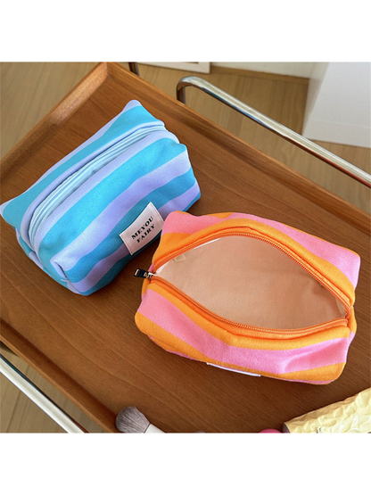 Open Orange striped makeup bag showing its pale peach lining beside a Turquoise bag