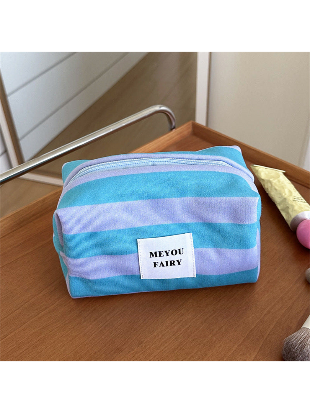 Turquoise striped makeup bag with light purple stripes and a white front label