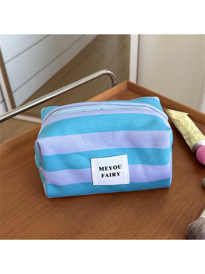 Turquoise striped makeup bag with light purple stripes and a white front label