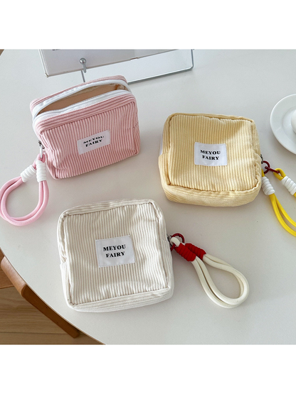 Pink makeup bag standing partly open beside Yellow and Beige wrist-loop bags