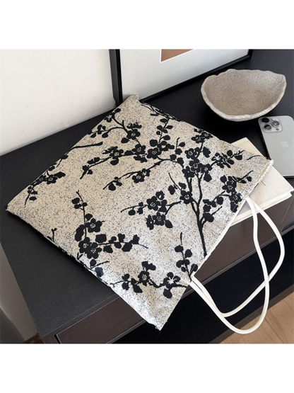 Black tote bag with flowering branches, laid diagonally with ivory loop handles