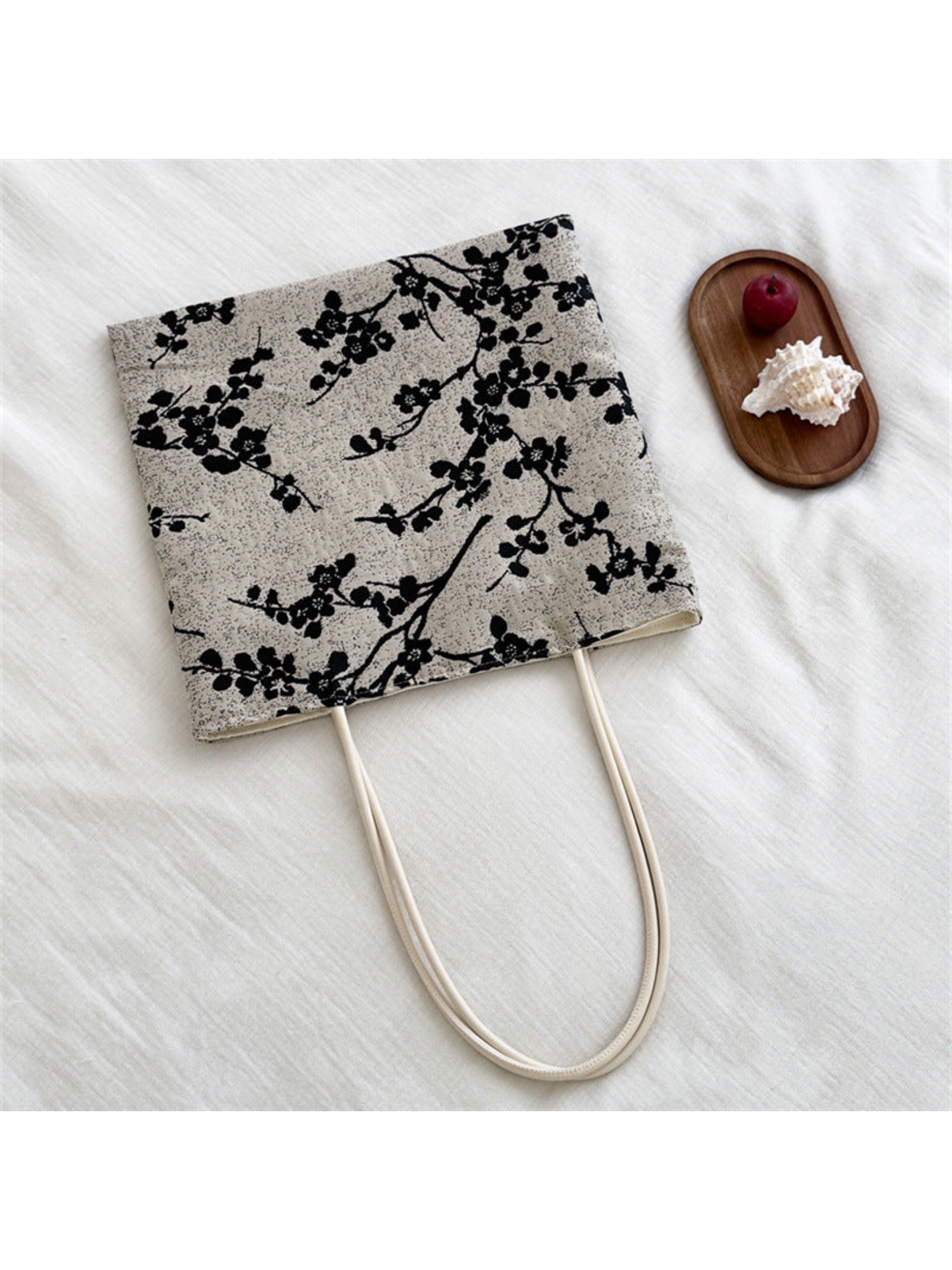 Black tote bag with flowering branches on a light speckled ground and ivory loop handles