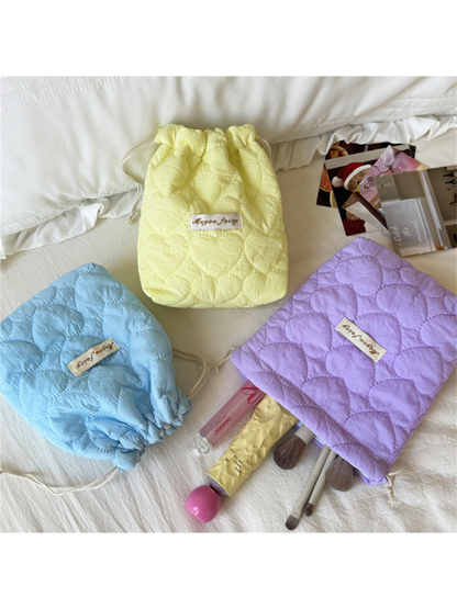 Yellow, Blue and Purple heart-quilted pouches with brushes and cosmetics beside the Purple opening