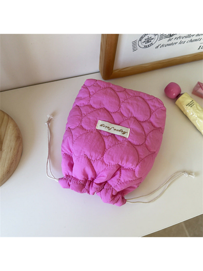 Fuchsia heart-quilted drawstring pouch with cream cords on a tabletop