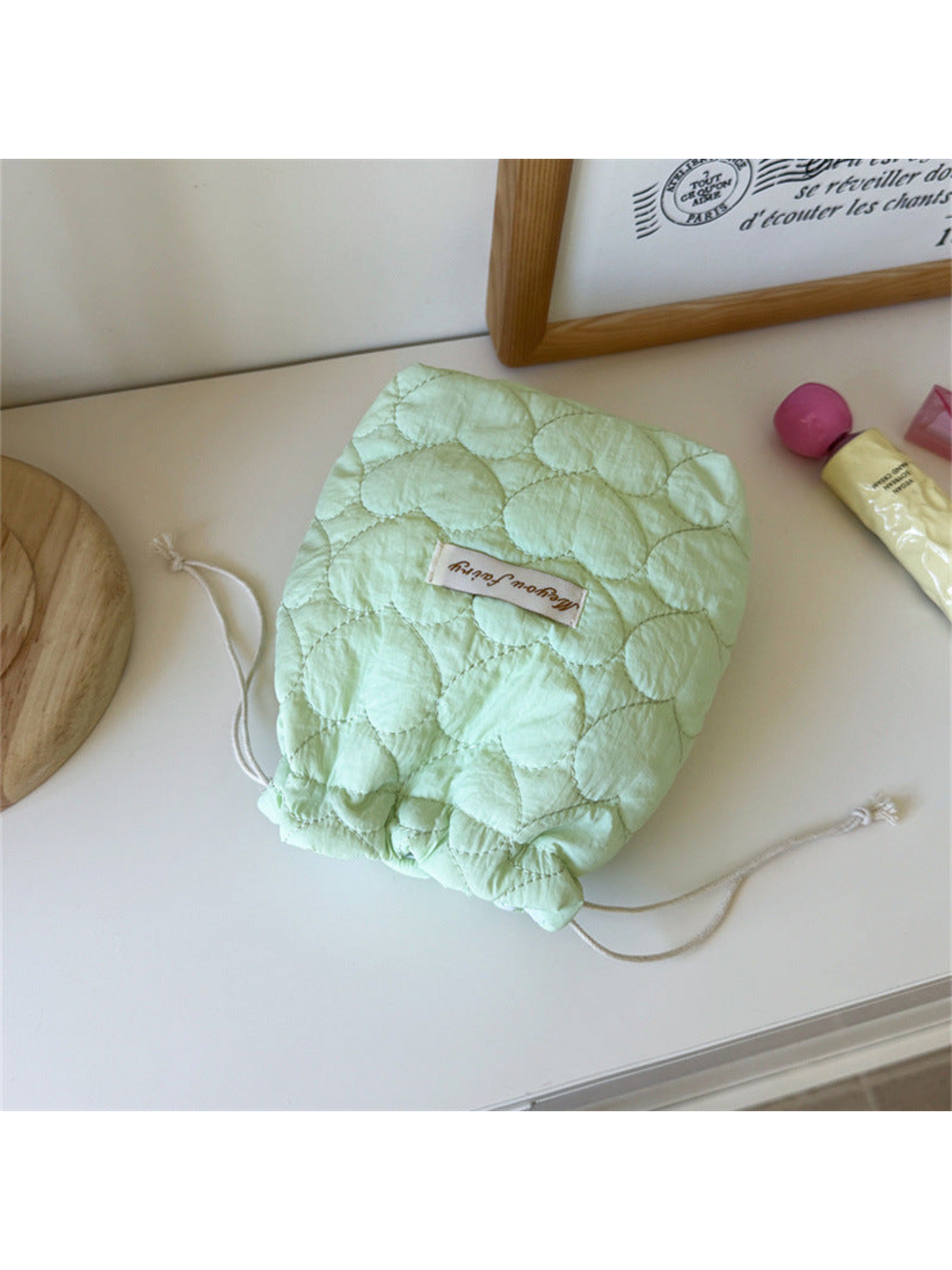 Mint heart-quilted drawstring pouch with cream cords on a tabletop