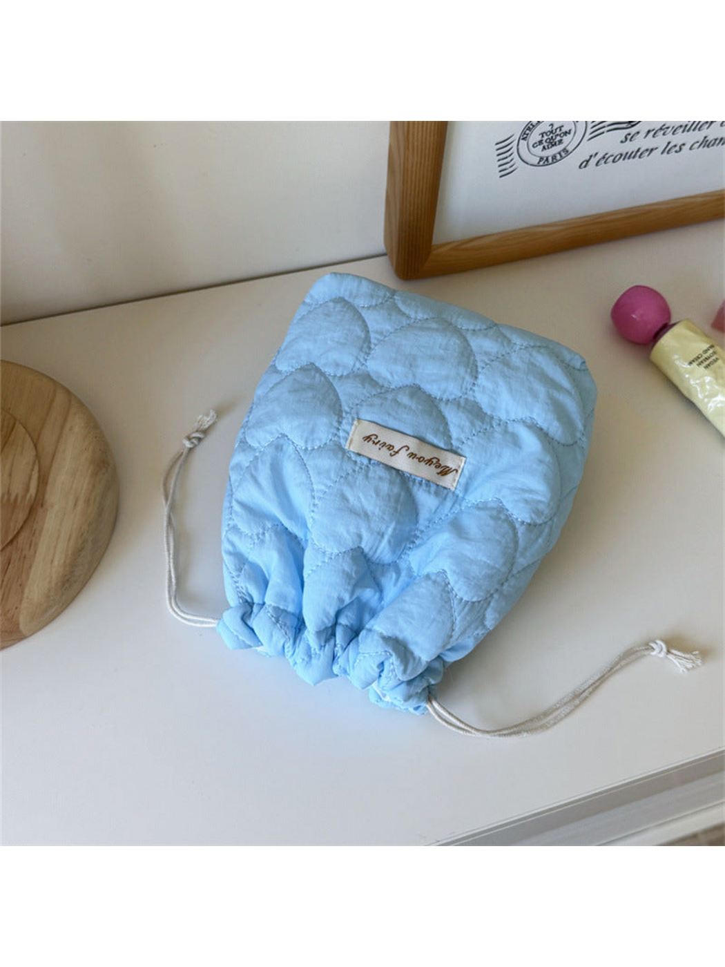 Blue heart-quilted drawstring pouch with cream cords on a tabletop