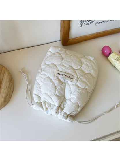 Ivory heart-quilted drawstring pouch with cream cords on a tabletop