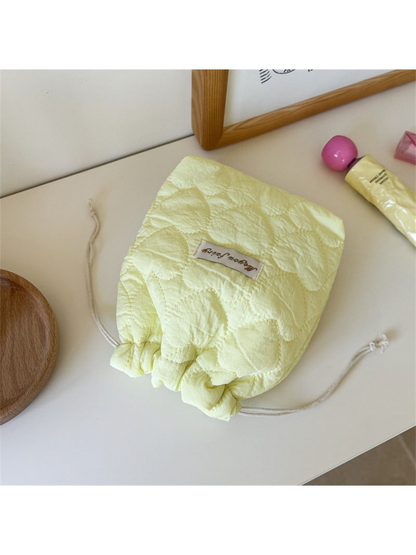 Yellow heart-quilted drawstring pouch with cream cords on a tabletop