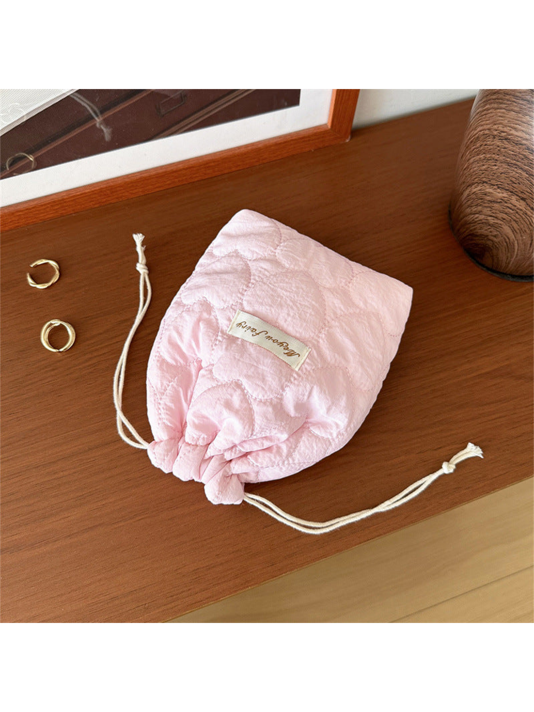 Pink heart-quilted drawstring pouch with cream cords on a wooden tabletop
