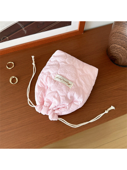 Pink heart-quilted drawstring pouch with cream cords on a wooden tabletop