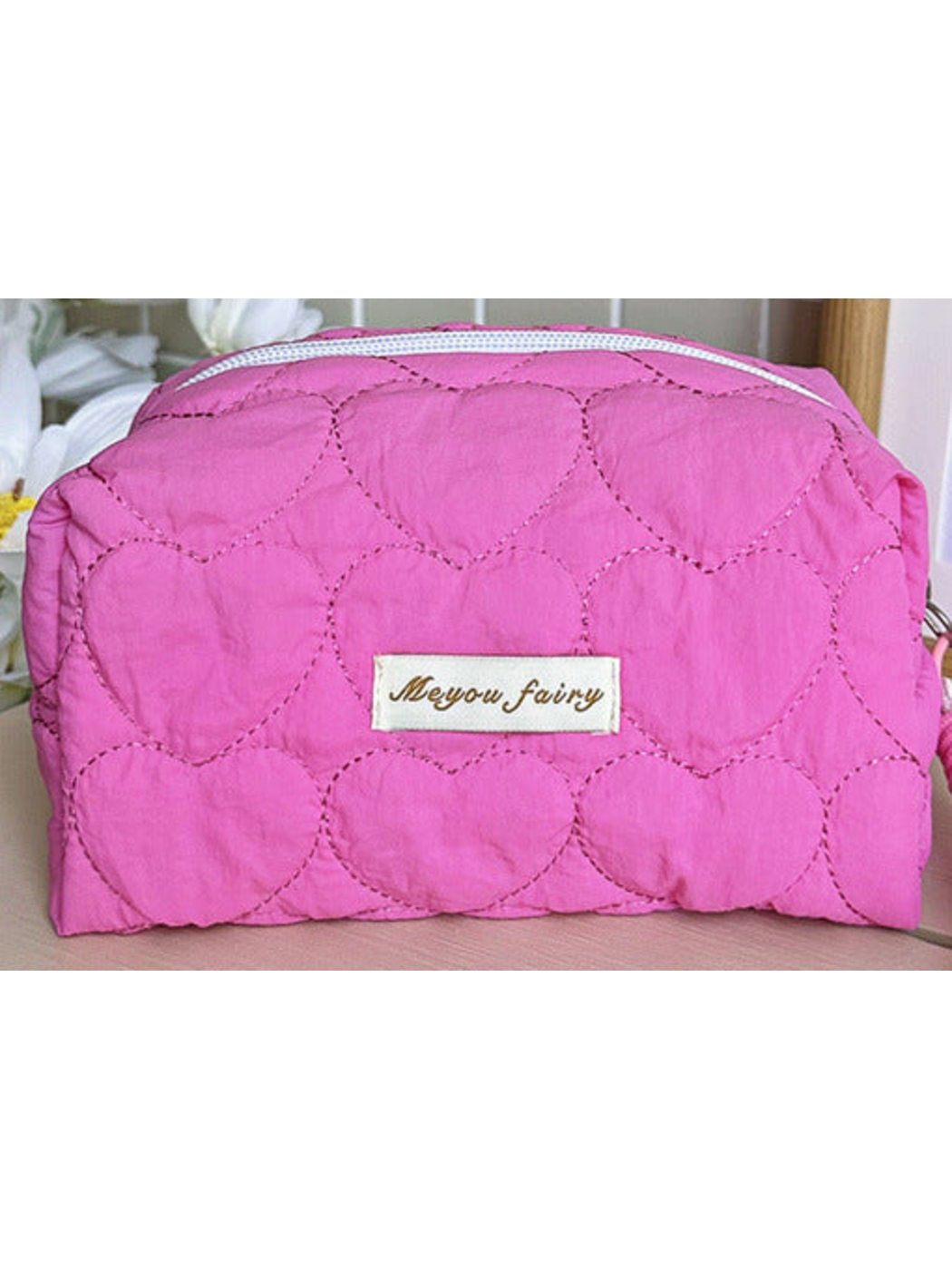 Pink heart-quilted pouch body with white zipper and sewn label; limited detail view